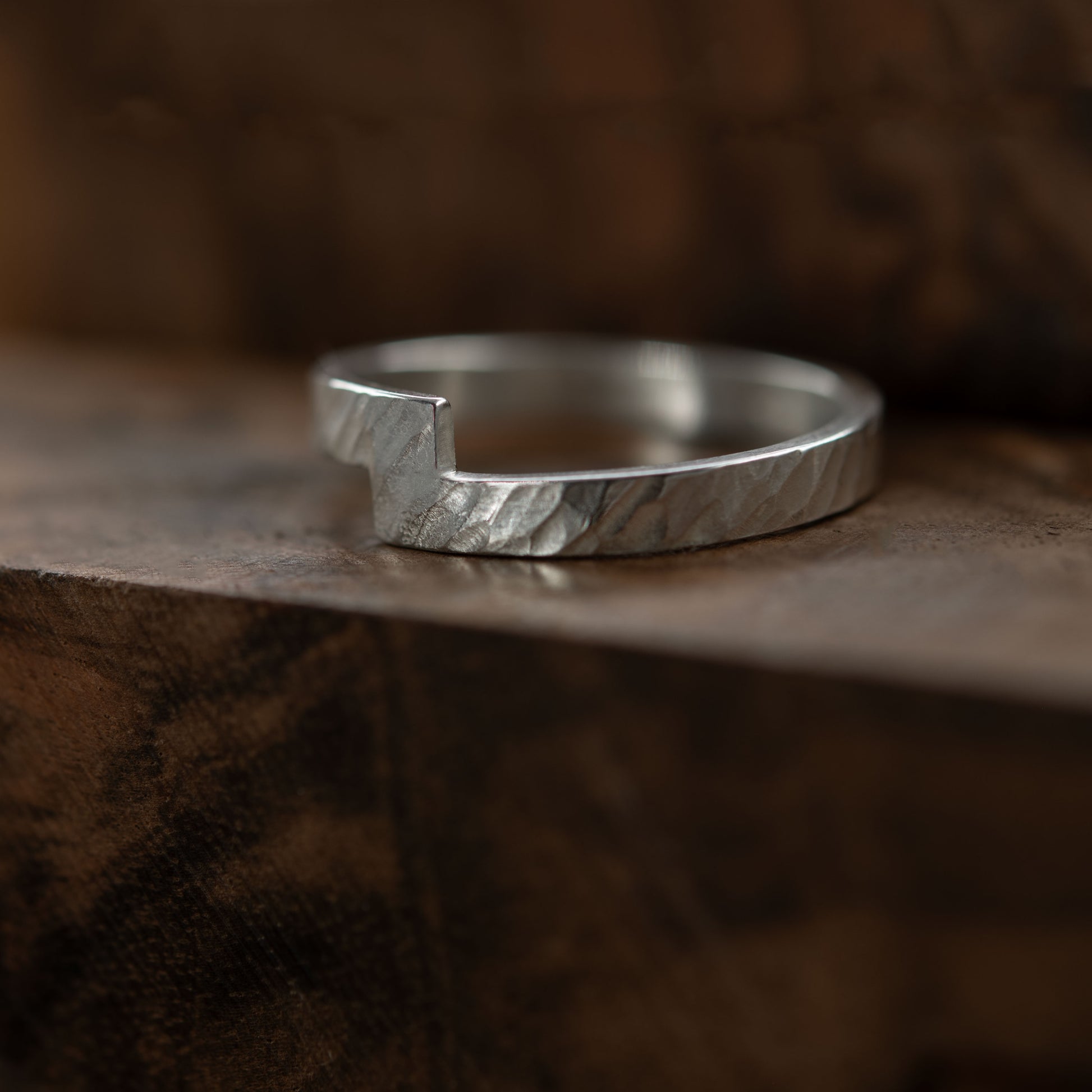 Close-up of a handmade hammered Unity ring made from sterling silver. The ring features a distinct zigzag design and is displayed on a textured wooden surface, highlighting its unique craftsmanship and modern aesthetic.