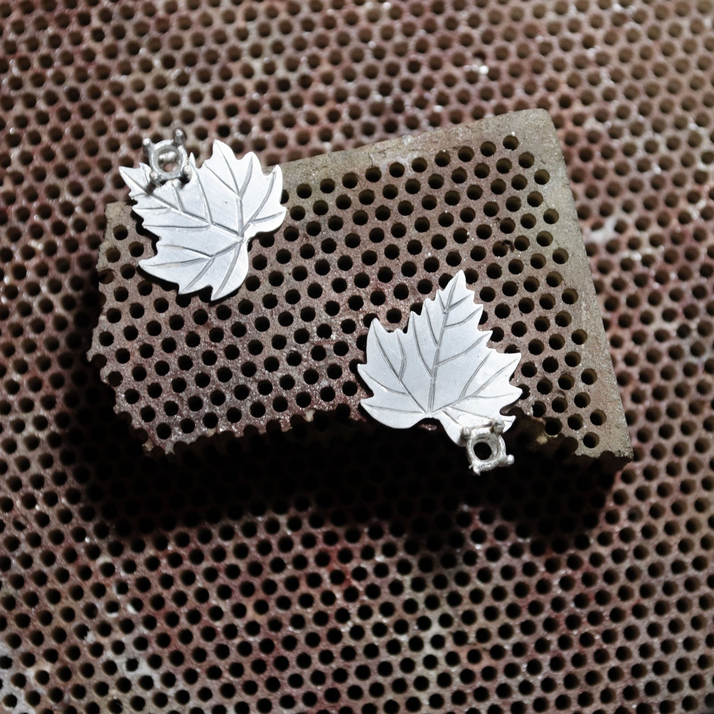 Silver leaf earrings in the making on a textured brown surface