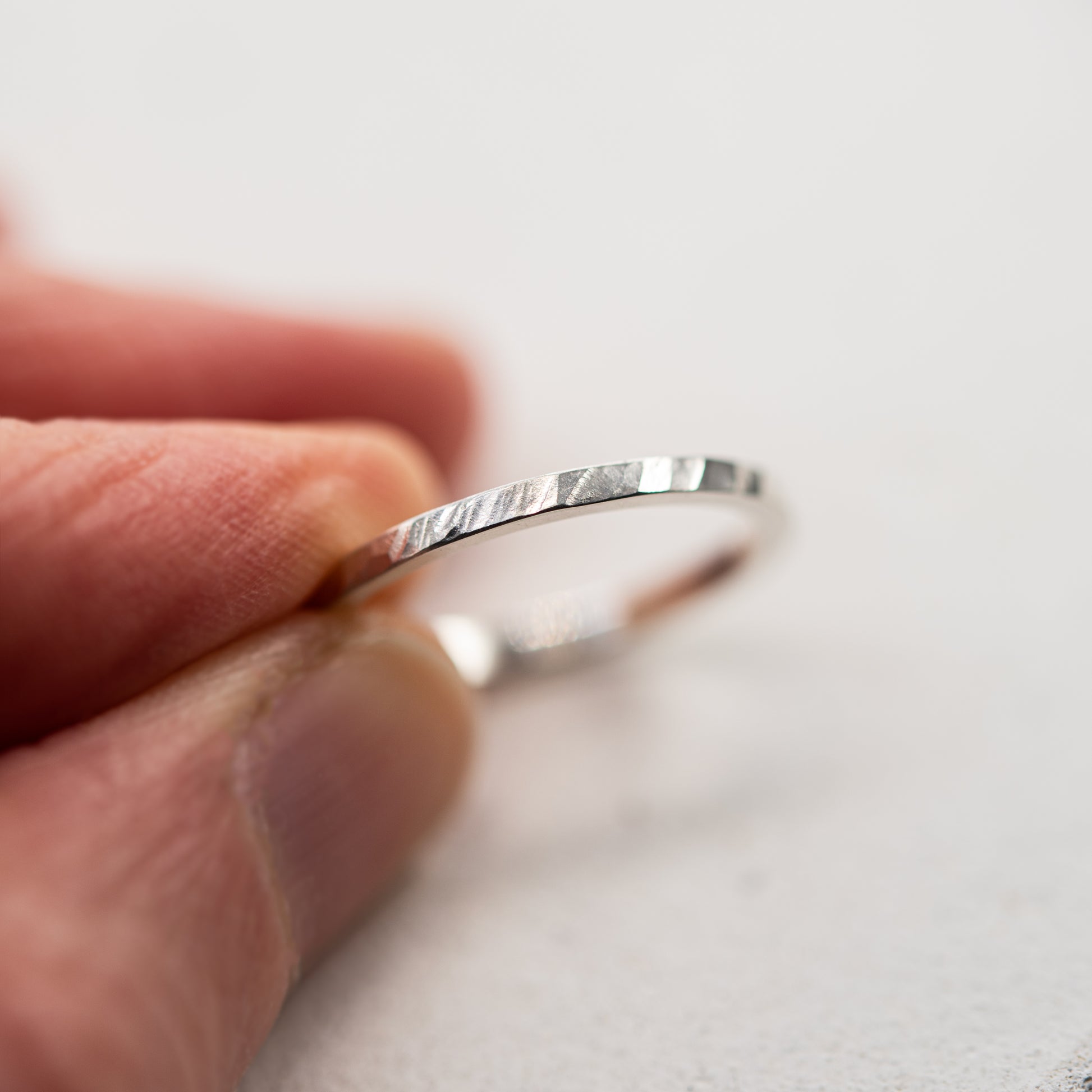 Gros plan d'une bague martelée fine en argent massif 925 au fini facetté, tenue entre les doigts sur fond clair.