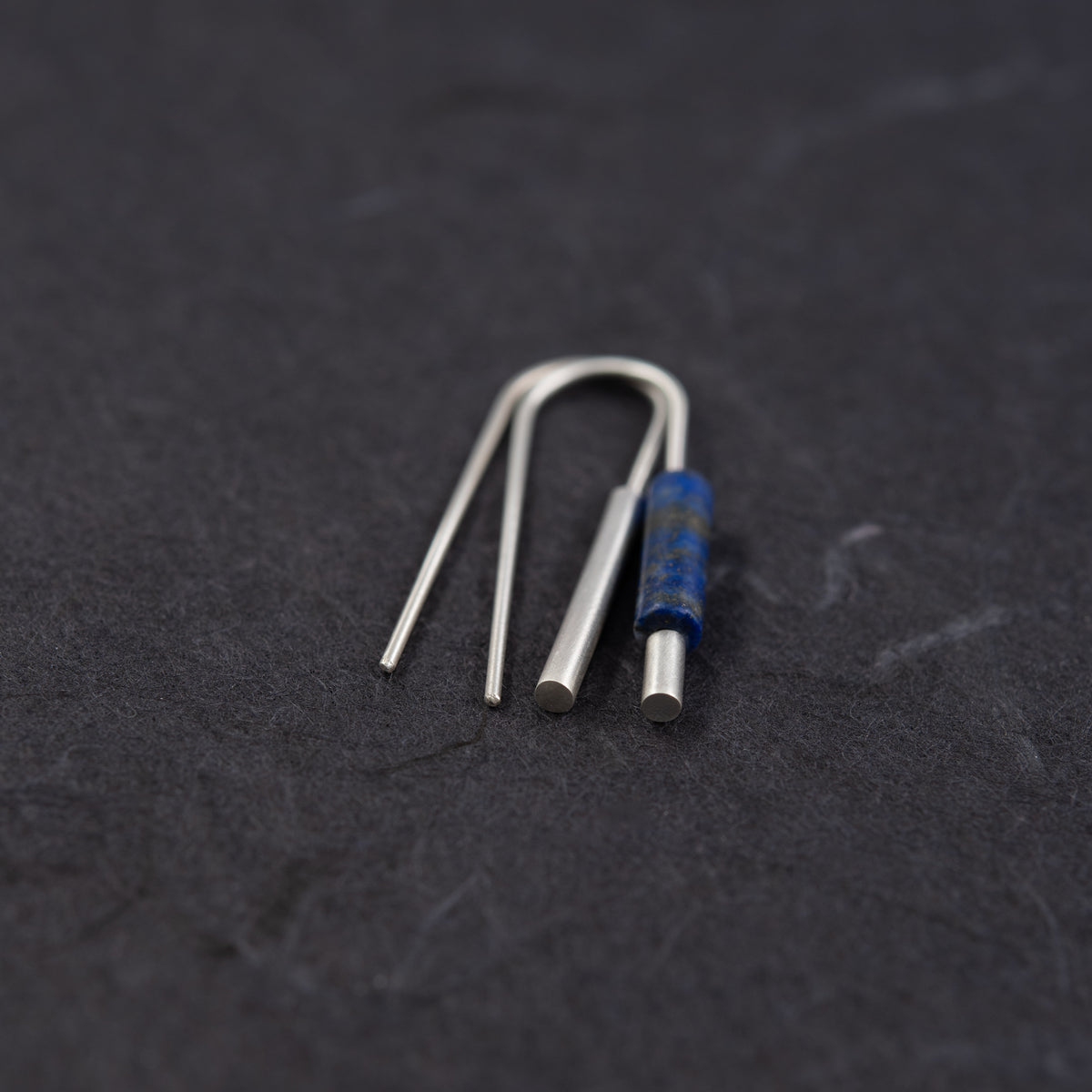 Minimalist sterling silver earrings with a cylindrical blue lapis lazuli detail.