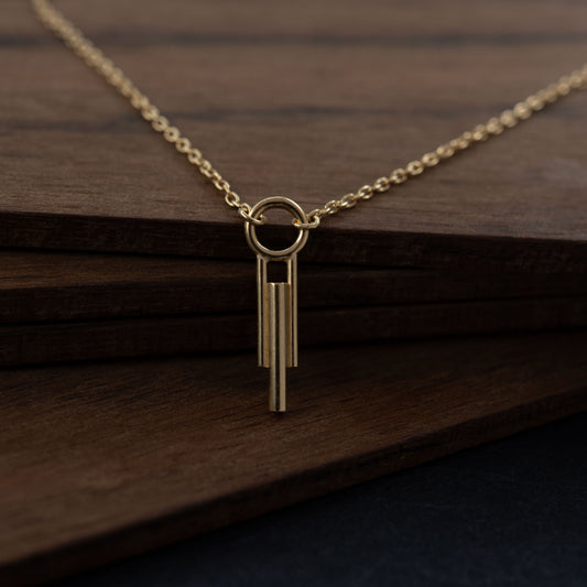 Gros plan d'un pendentif cylindrique Art Déco à trois barres avec chaîne en vermeil  contre fond de bois foncé, bijou fait main à Paris