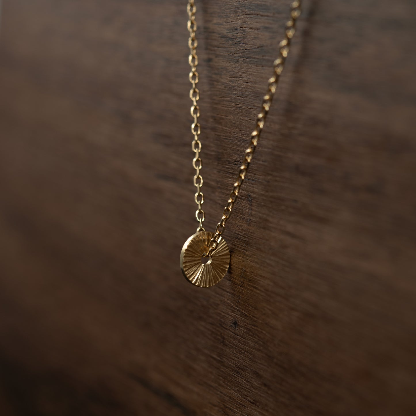 Détail du pendentif Soleil en vermeil gravé à la main révélant les reflets de sa texture artisanale.