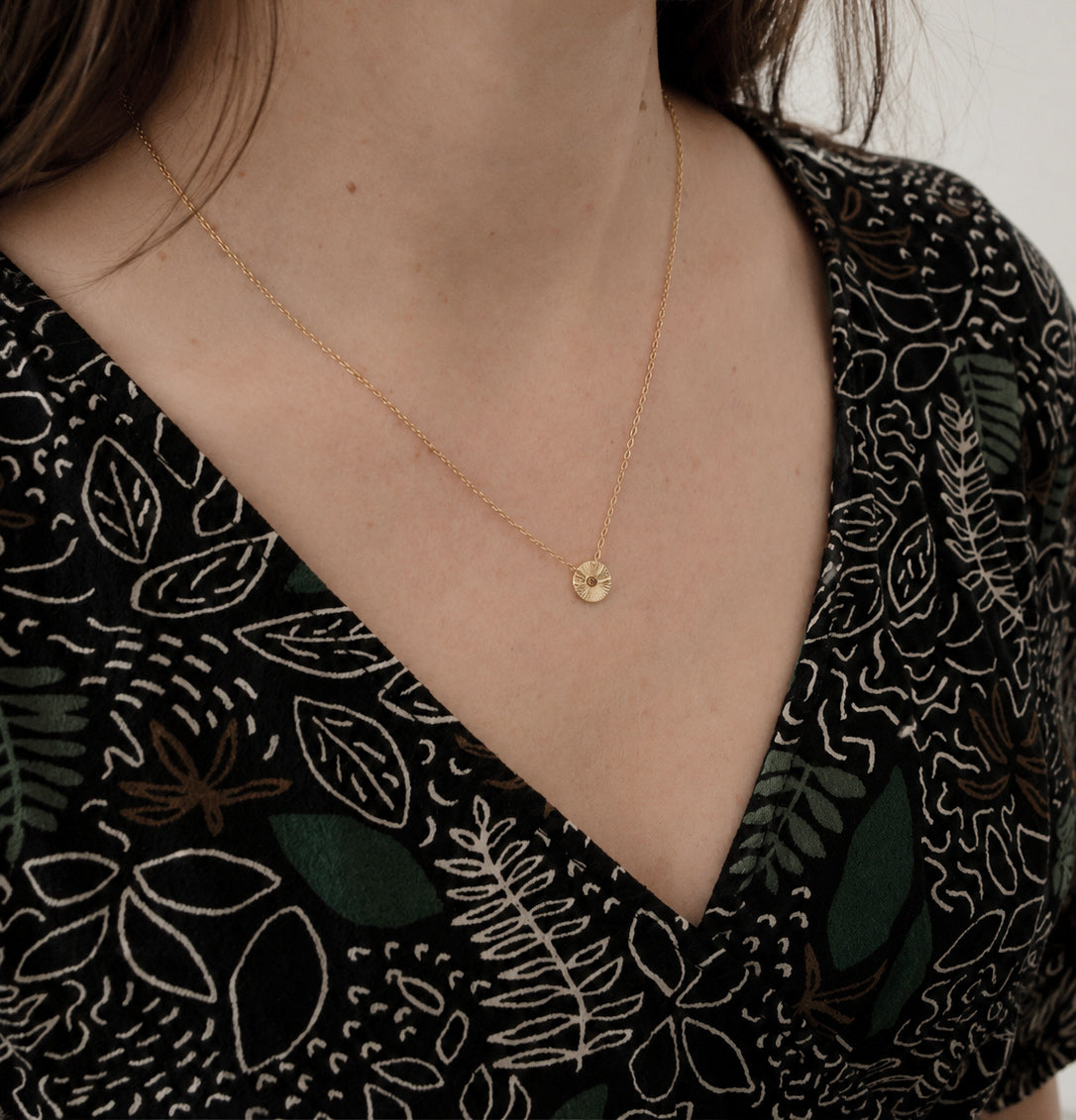 Femme portant un collier Soleil en vermeil avec un petit pendentif rond gravé à la main sur une fine chaîne. Bijou minimaliste fabriqué à la main dans notre atelier parisien.