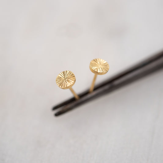 Gros plan de petites boucles d’oreilles clous en vermeil or gravé sur fond gris clair – bijou artisanal minimaliste de Paris