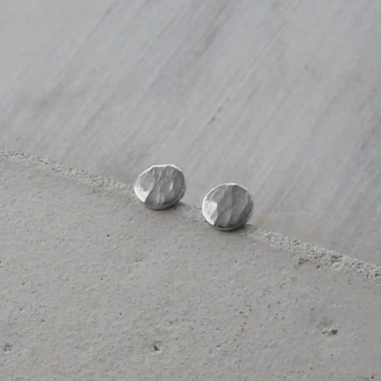 Vidéo montrant une paire de petites boucles d'oreilles en argent martelé. Les boucles d'oreilles sont mises en valeur sous différents angles, révélant leur texture brillante et leur finition artisanale. La vidéo illustre la légèreté et l'élégance des bijoux, accompagnée d'un fond neutre qui permet de se concentrer sur les détails des boucles d'oreilles.