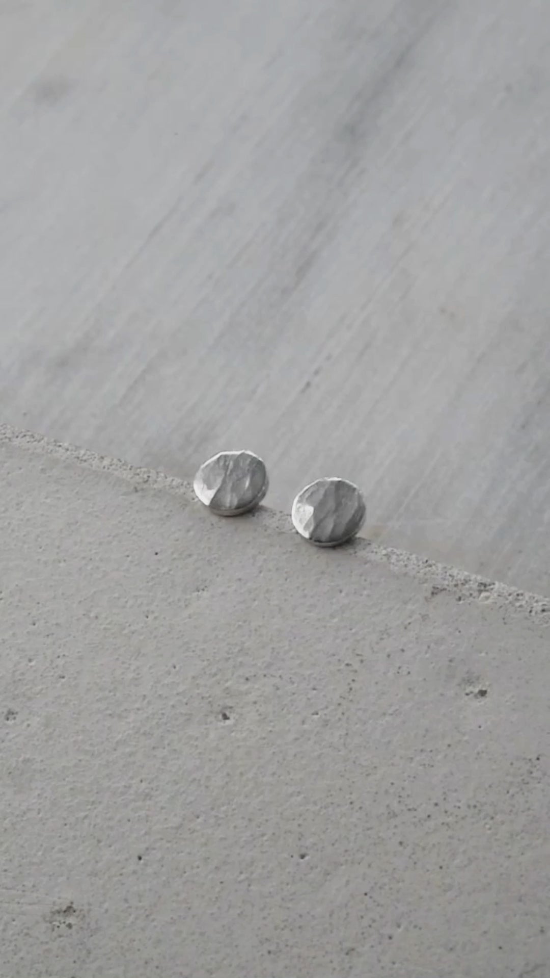 Vidéo montrant une paire de petites boucles d'oreilles en argent martelé. Les boucles d'oreilles sont mises en valeur sous différents angles, révélant leur texture brillante et leur finition artisanale. La vidéo illustre la légèreté et l'élégance des bijoux, accompagnée d'un fond neutre qui permet de se concentrer sur les détails des boucles d'oreilles.