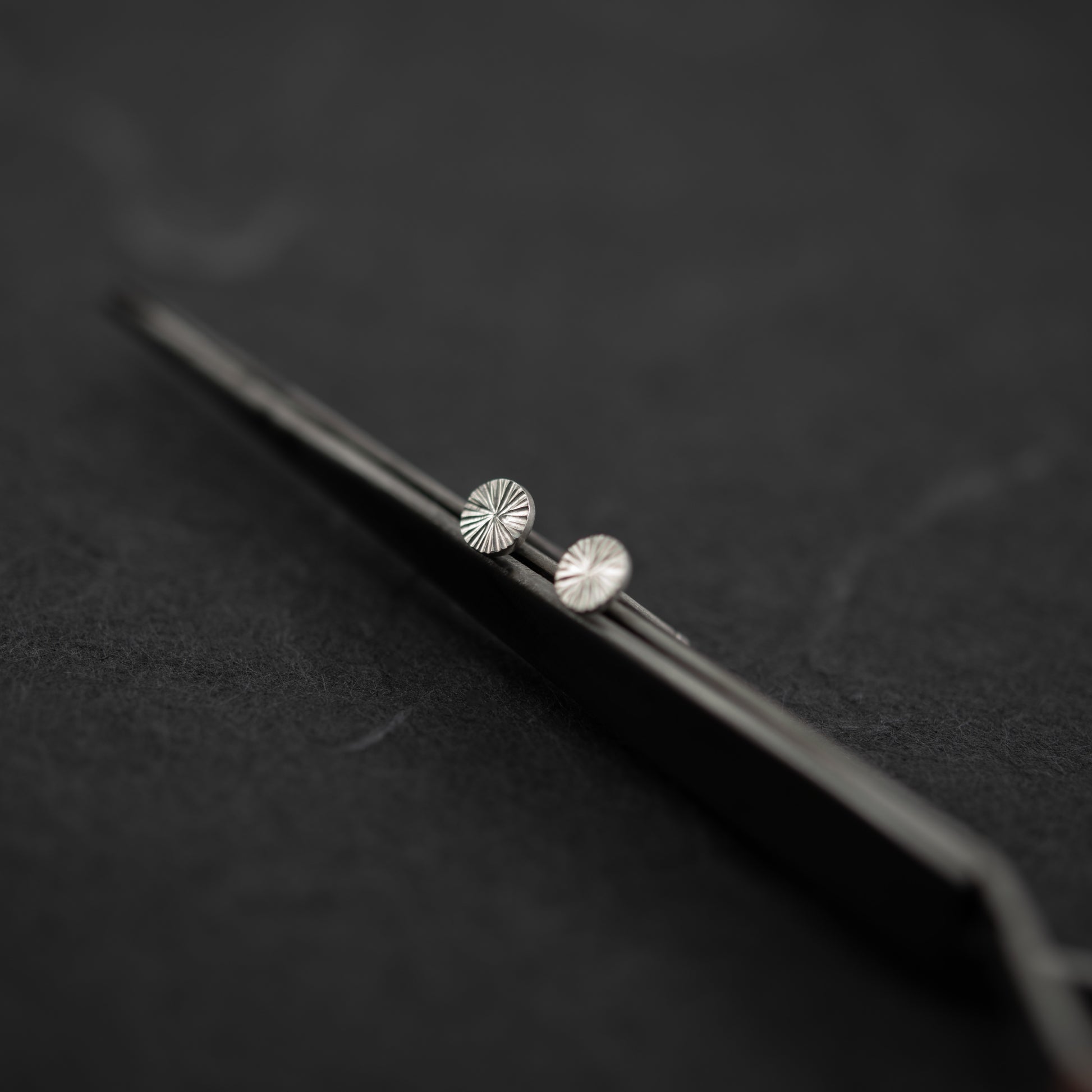 Puces d’oreilles en argent massif gravées à la main, design rond minimaliste 5 mm captant la lumière sur une surface grise