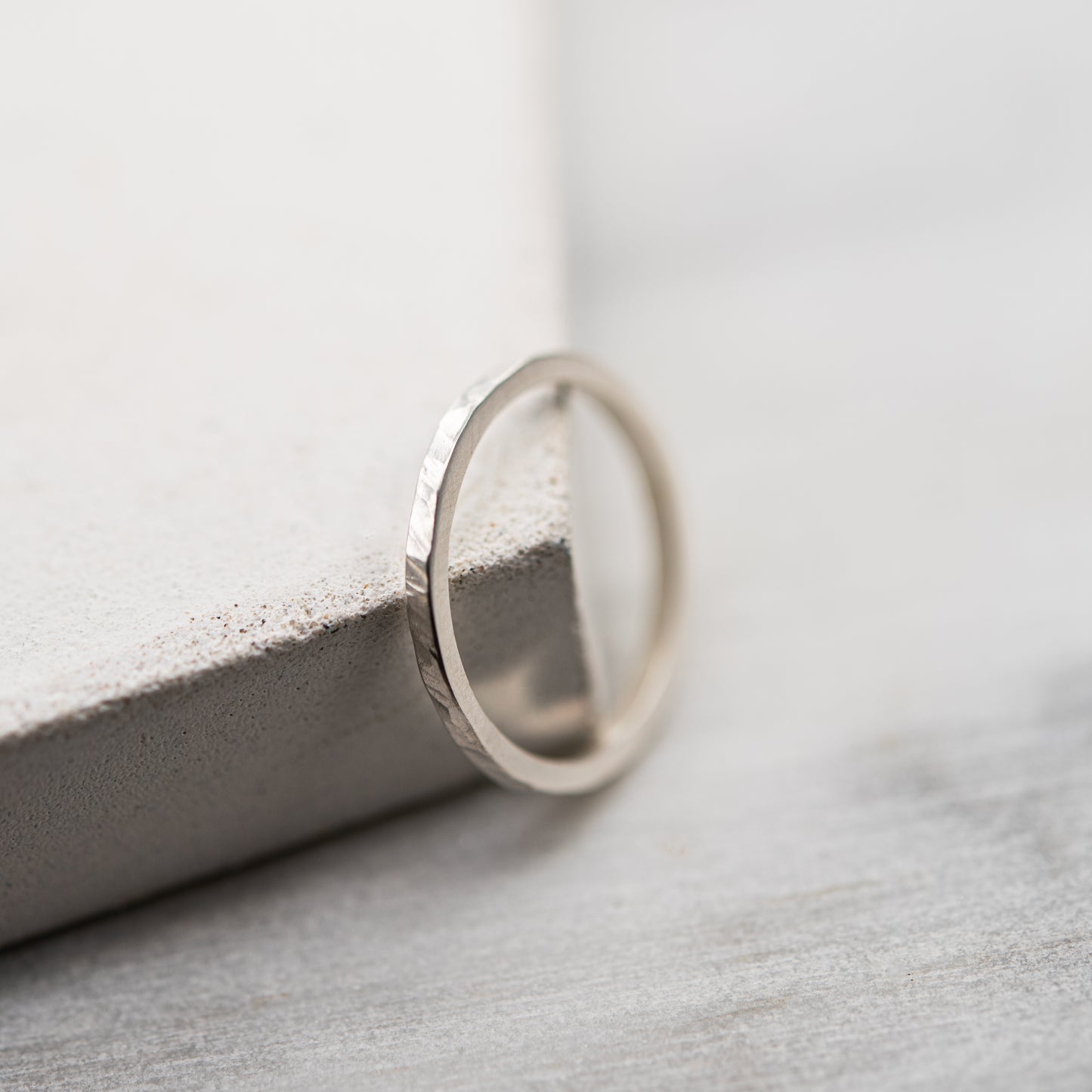 Vue de profil d'une bague martelée fine en argent massif 925, posée contre un support en béton clair sur fond minéral.