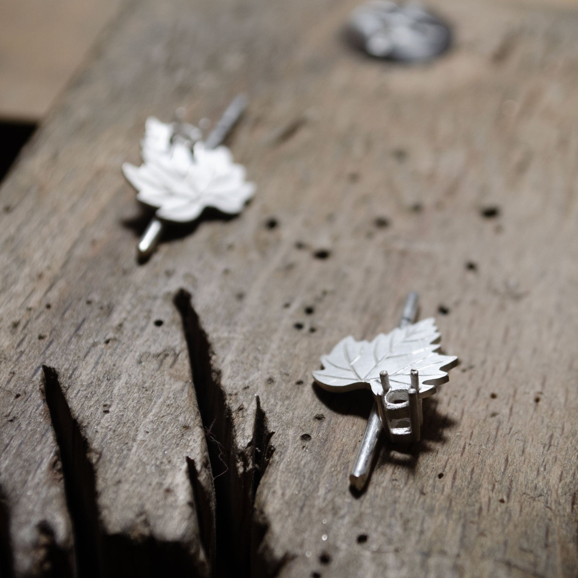 A close-up view of silver earring in the shape of a leaf being made on a wooden surface