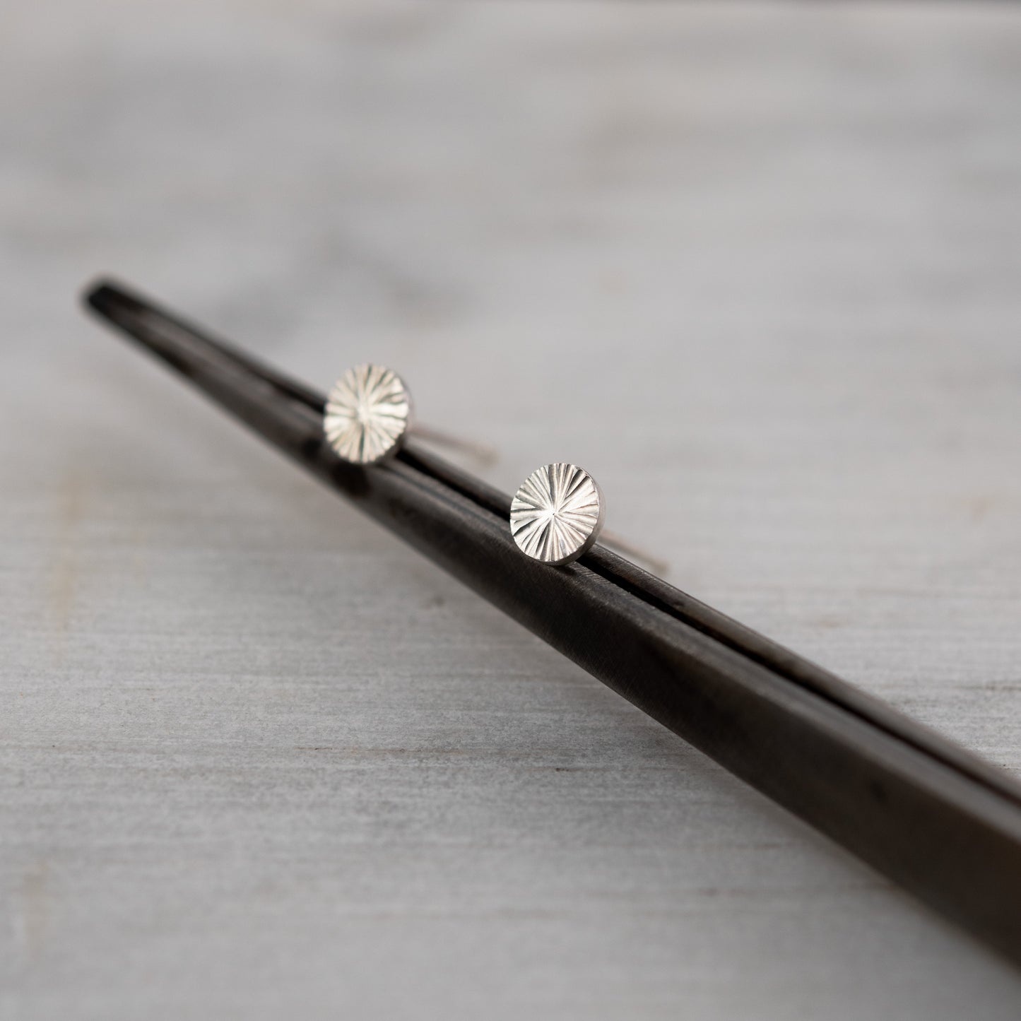 Hand-engraved sterling silver stud earrings, minimalist 5mm round design reflecting lighton a gray surface