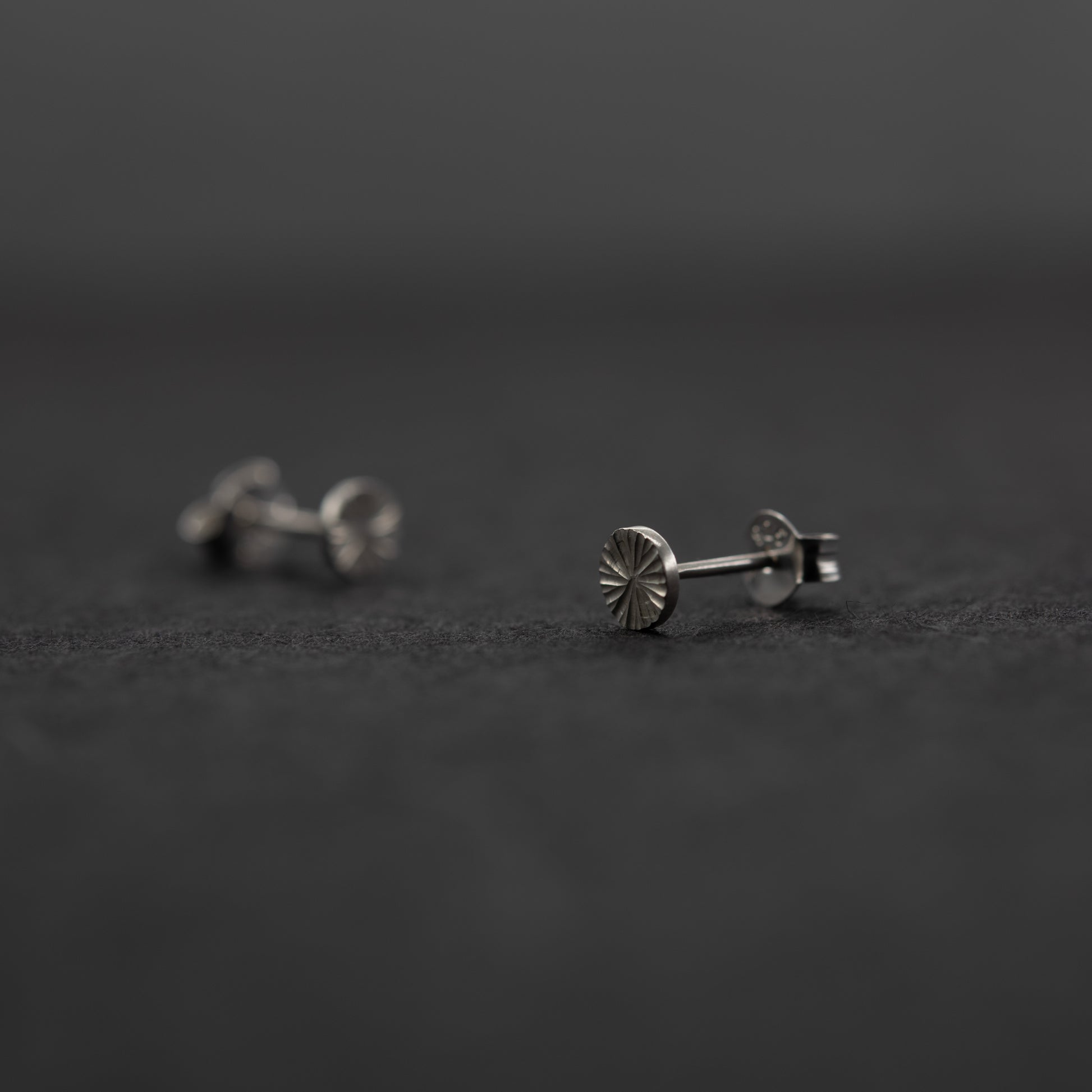 Artisan sterling silver stud earrings, subtle light-catching engraved finish on a dark background