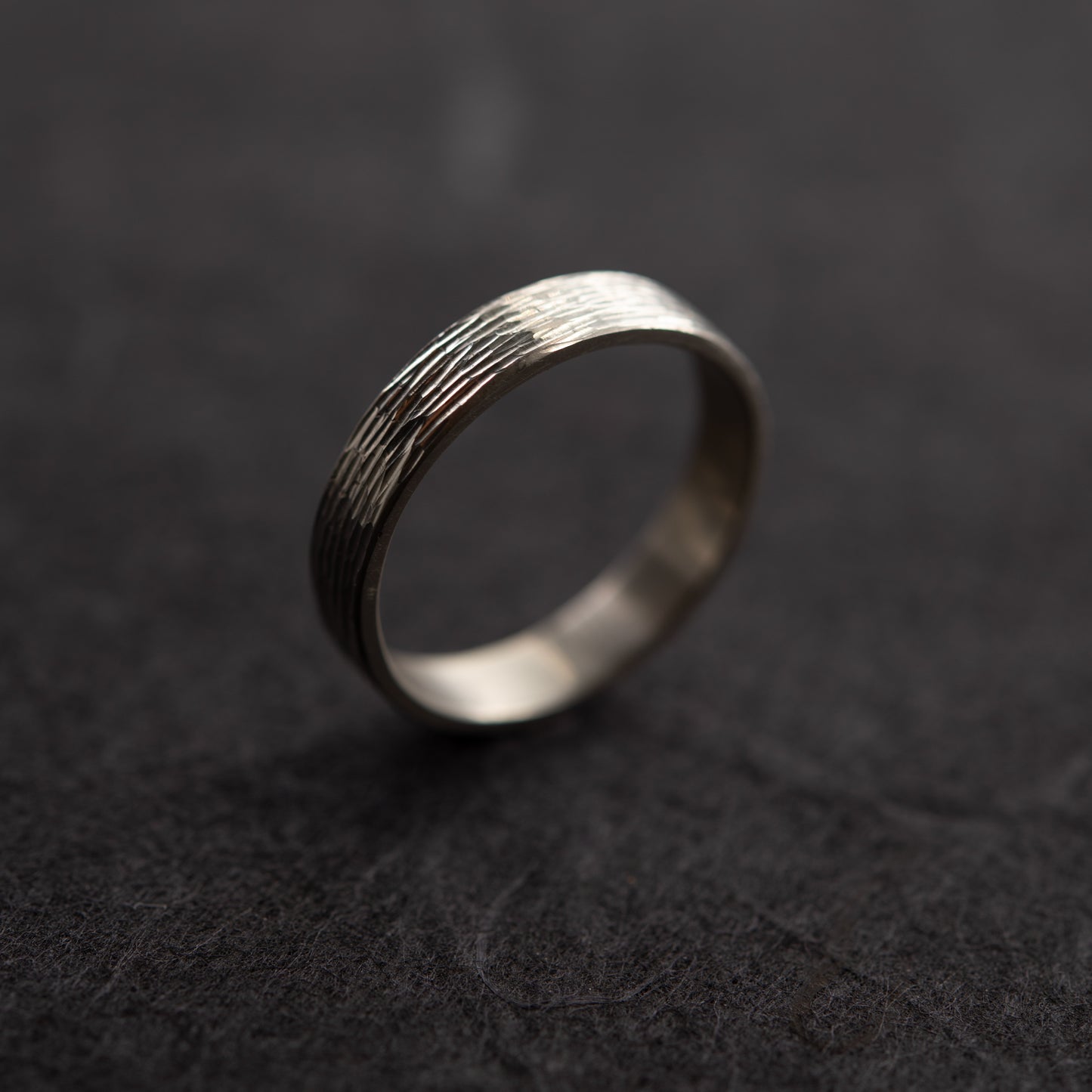 Detailed view of sterling silver wedding band with hand-engraved texture on dark background, handmade in paris by agjc. 