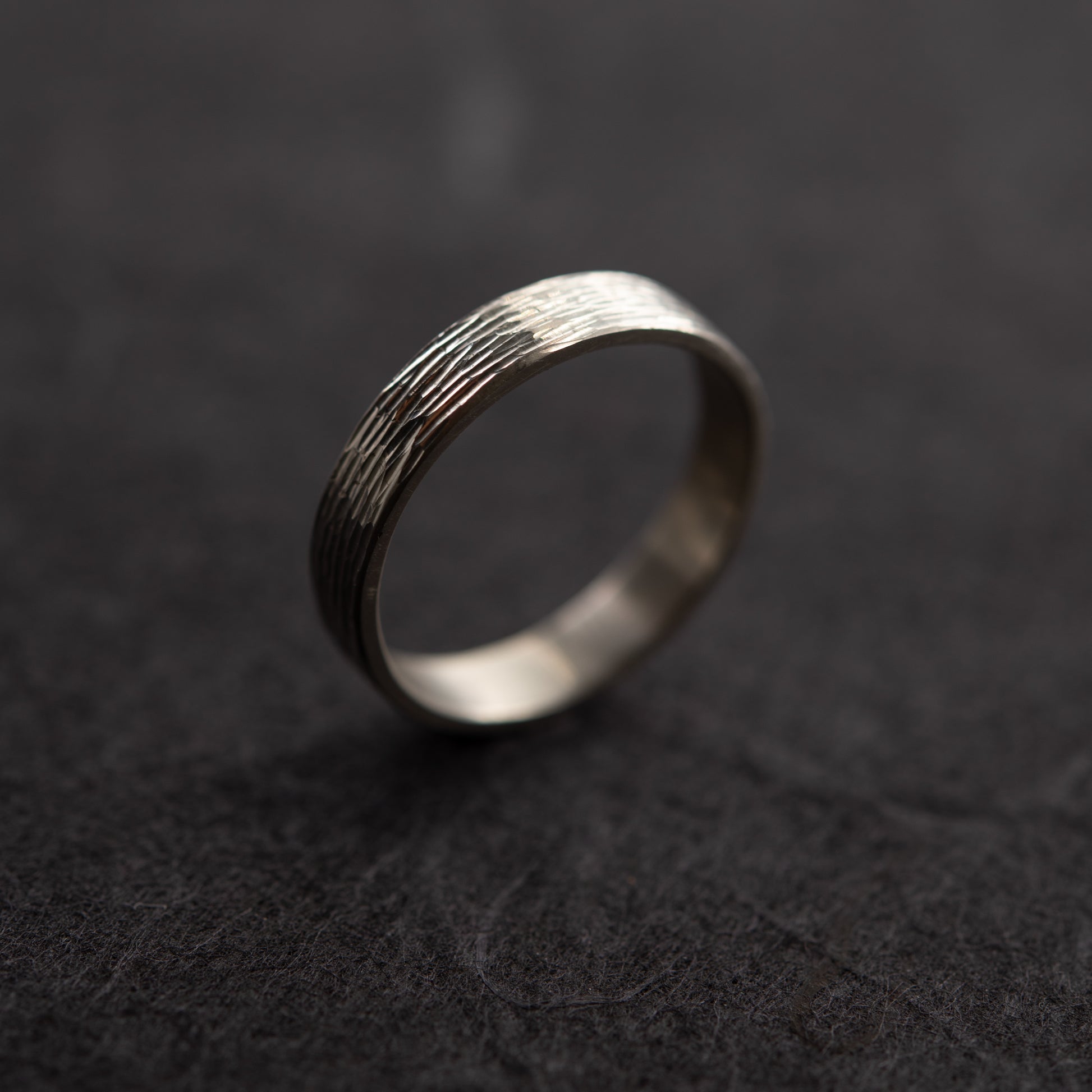 Detailed view of sterling silver wedding band with hand-engraved texture on dark background, handmade in paris by agjc. 