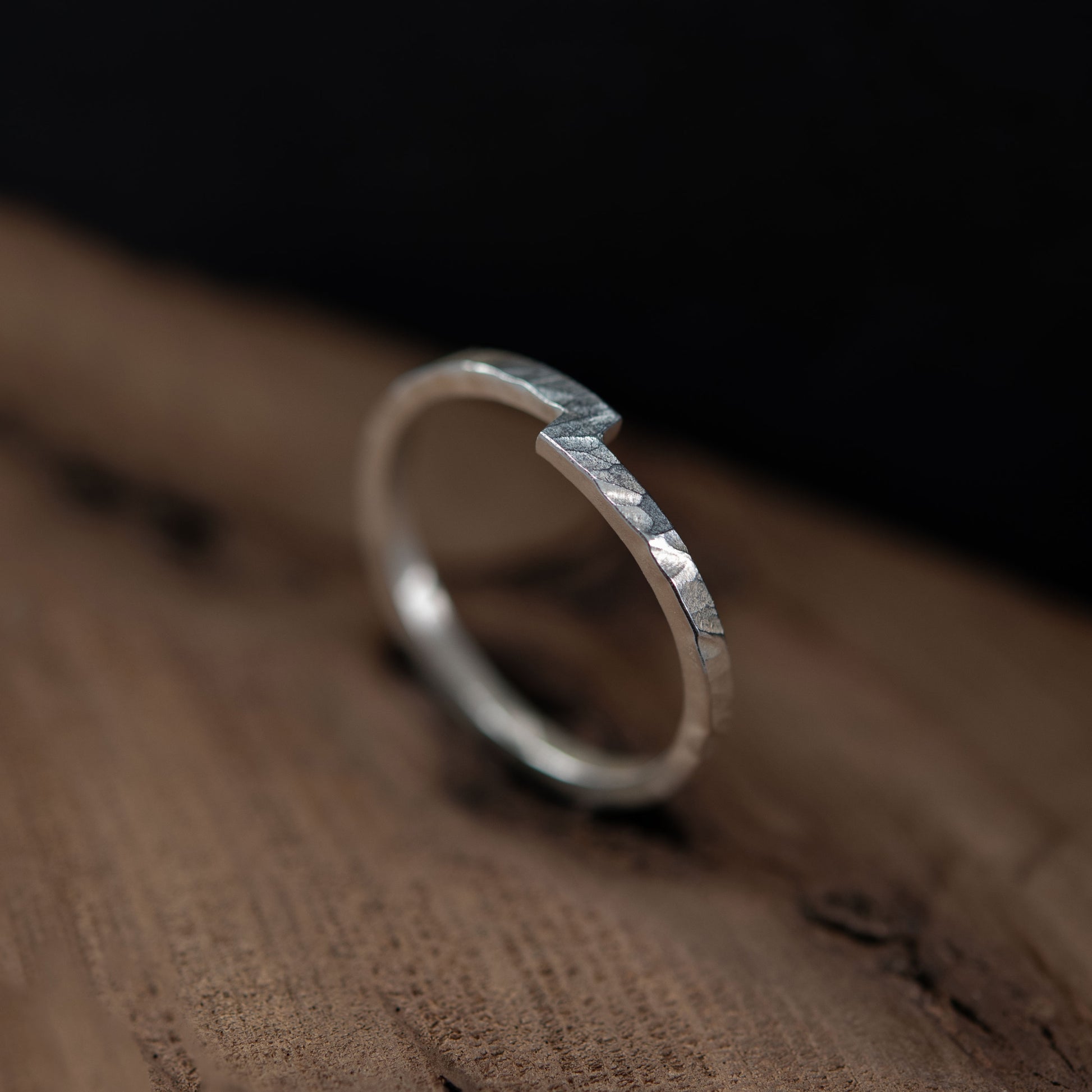 Sterling silver hammered ring placed on a wooden surface, featuring a unique design that symbolizes the union of two elements. This minimalist ring showcases a distinctive notch detail, representing connection and harmony, making it an ideal choice for a wedding band, engagement ring, or meaningful everyday accessory. A modern and timeless handmade piece.
