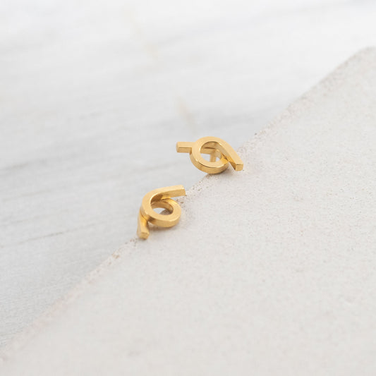 Close-up view of a pair of minimalist Vermeil stud earrings, featuring a unique design with intertwined shapes. The earrings have a shiny finish and are positioned on a textured surface, showcasing their modern aesthetic.