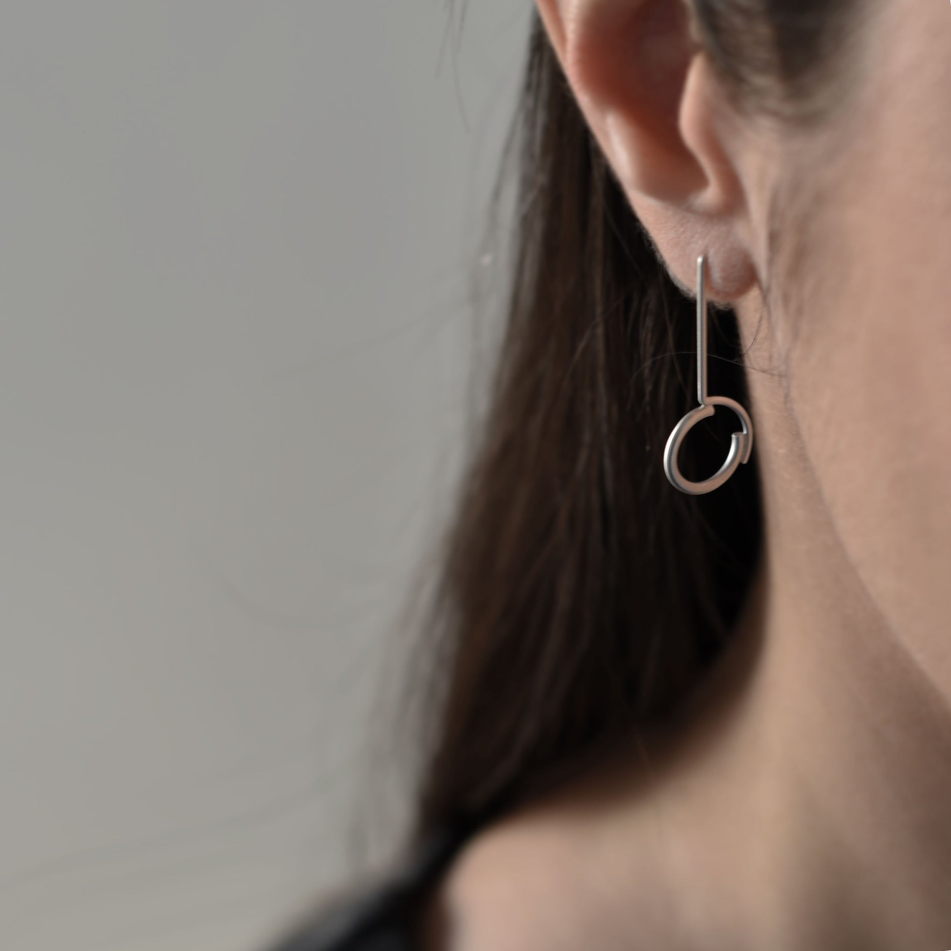 A half face of a woman wearing a circle pendant earring of 32 millimters in heght , handmade in matte silver