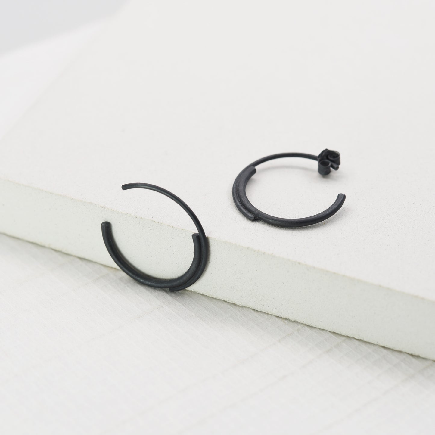 close up of a concentric circle small pair of hoops earrings in black oxidized silver in a white background