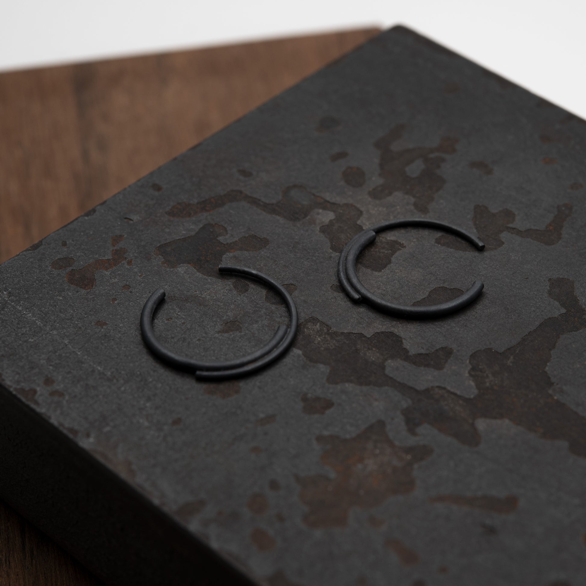 close up of a concentric circle small pair of hoops earrings in black oxidized silver in a brown background