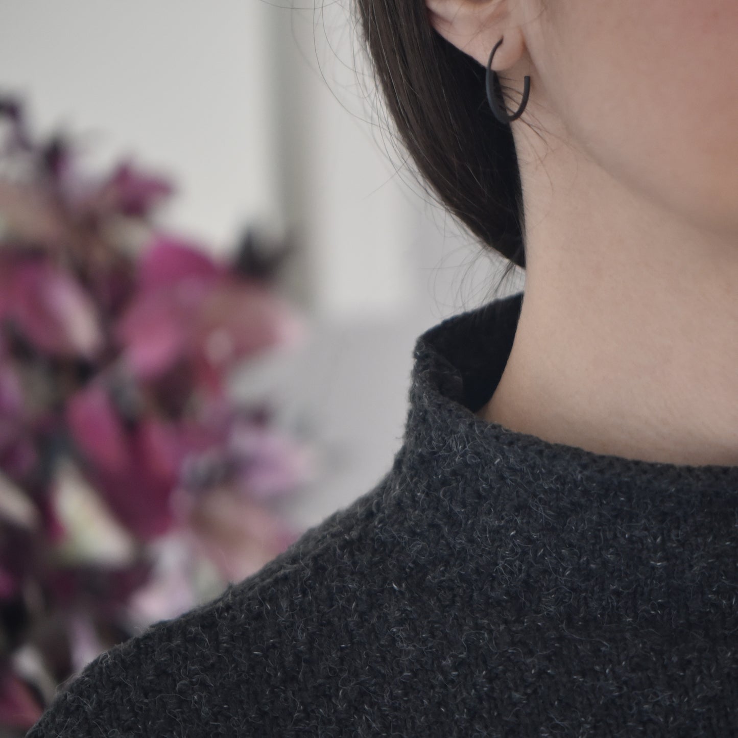 half face of a woman wearing a 22 millimeters diameter pair of hoops earrings in black oxidized silver in a white background