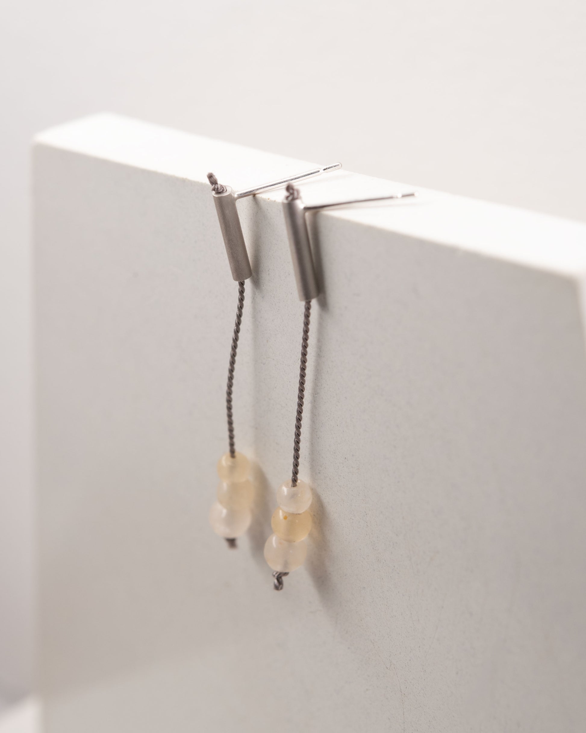 Pair of 42 millimeters length pendant earrings handmade in in Paris by A g J c  from  tube of matte sterling silver with a beige silk cord threaded through the center for hanging yellow quartz beads. 