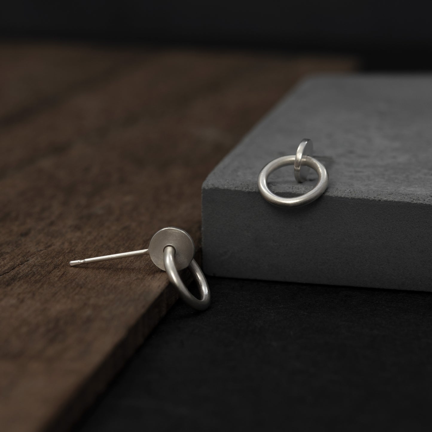 Close up of a a pair of silver matte studs designed with an interlocked dot and circle  The earrings measure 13 millimeters in length.