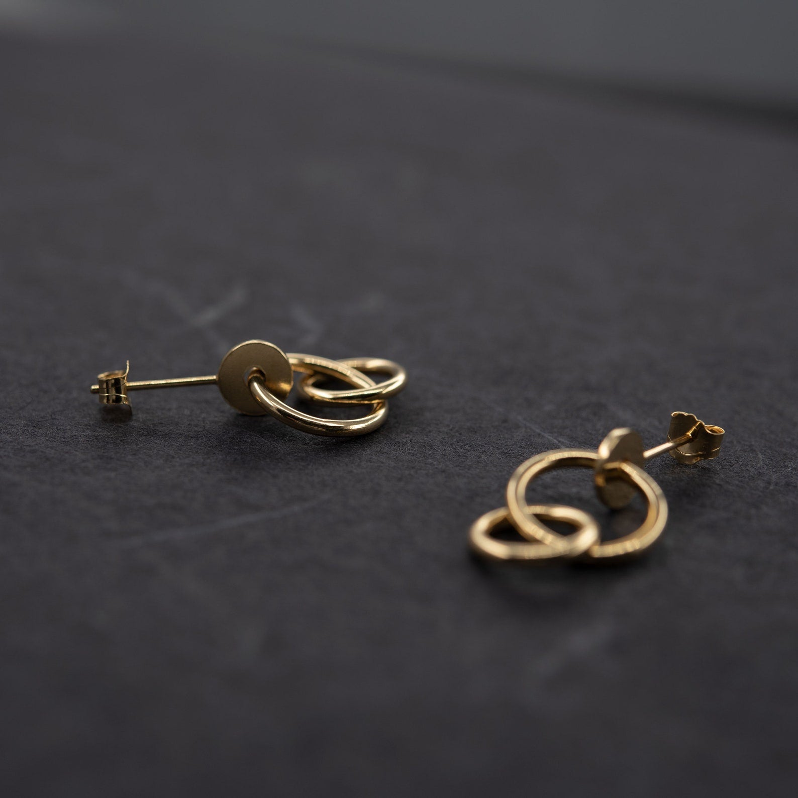 Pair of gold plated studs earrings designed with an interlocking dot and two hoops linked in shiny finish. Handcrafted by a g j c in Paris. The drop length measures 19 millimeters with a total earrings length of 22 millimeters. They can be worn on the ear lobe and attached with push backs. 