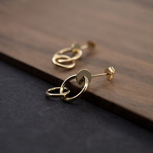 Pair of gold plated studs earrings designed with an interlocking dot and two hoops linked in shiny finish. Handcrafted by a g j c in Paris. The drop length measures 19 millimeters with a total earrings length of 22 millimeters. They can be worn on the ear lobe and attached with push backs. 